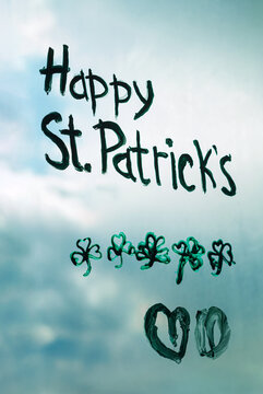 Drawing St. Patrick's Day painting green three-leaved shamrocks indoor, festive home decoration, quarantine family leisure. Child draws clovers and hearts on window glass. Stay home concept New normal