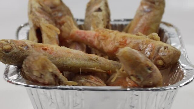 A closeup of cleaned and fried fresh small mullets in a foil plate in 4K