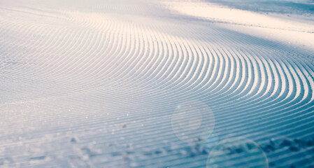Close up of groomed tracks on a slope in a downhill ski resort on a sunny day. Shallow depth of field.