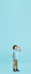 Pointing up, choosing. Childhood and dream about big and famous future. Pretty little boy isolated on blue studio background. Dreams, imagination, education, facial expression, emotions concept. Flyer