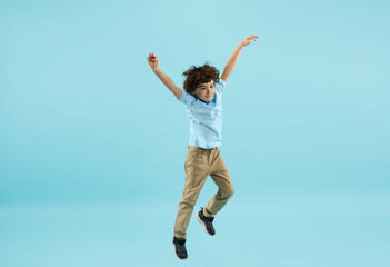Fototapeta premium Flying, jumping high. Childhood and dream about big and famous future. Pretty little boy isolated on blue studio background. Dreams, imagination, education, facial expression, emotions concept.