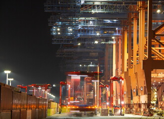 Cranes in the container harbour port during logistic loading process at night time with artificial...
