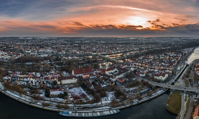 Panorama der Stadt Regensburg in Bayern mit dem Fluss Donau dem Dom und der steinernen Brücke im Winter mit Schnee und Eis während Sonnenuntergang, Deutschland