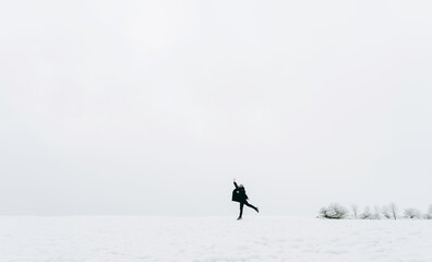 Naklejka na ściany i meble A happy female person jumps on the background of a winter snow-white landscape.The winter lifestyle.A small man against the background of a large nature.Minimal, stylish concept