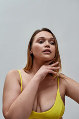 Portrait of beautiful curvy young woman wearing yellow underwear looking away, posing isolated over grey background