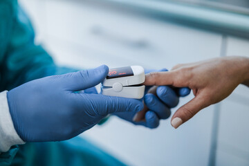 Doctor examining patient with fingertip pulse oximeter during coronavirus outbreak - Soft focus on left hand