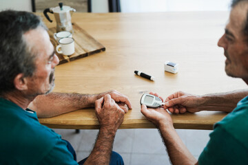 Senior twin men making blood glycemia test for diabetes check - Focus on hand holding glucometer