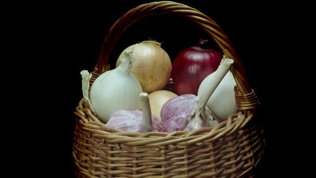 Composition of vegetables, rotation of a basket with onions and garlic on a black background