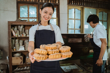 smiling girl making a cake wearing an apron carrying a plate of cake with a man opening the oven as a background