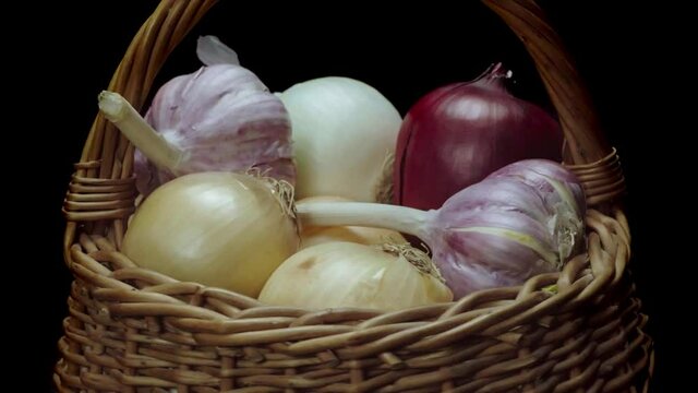 Composition of vegetables, rotation of a basket with onions and garlic on a black background