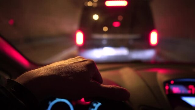 Waiting for movement by car in a traffic jam tunnel. The driver's hand holds the steering wheel. Patience while waiting to move. Passenger transportation. Cars are driving in bokeh.