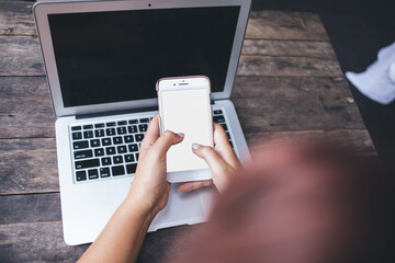 Unrecognizable woman messaging via cellphone while resting at wooden table with laptop