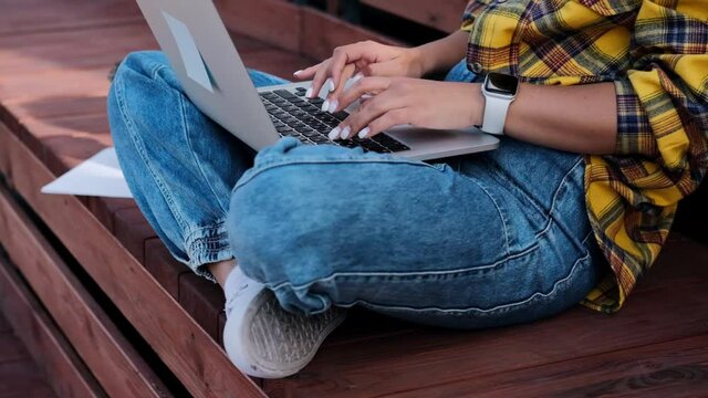 Close up of woman typing on laptop keyboard sitting on roof terrace on summer sunny day.