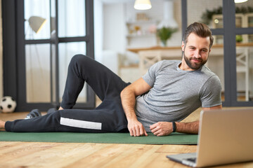 Fototapeta na wymiar Handsome young man lying on yoga mat and using laptop