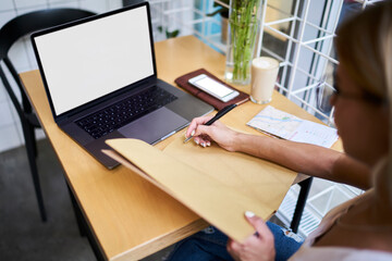 Crop faceless woman working on laptop and taking notes