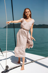Full-length portrait. Very cute and pretty girl in a long gray dress posing on a white yacht and looking directly at the camera against the background of the water. Summer holiday concept.