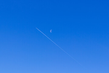 The trail of the plane and the moon on a blue background