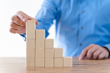 Businessman hand arranging wooden blocks in an upward stepping stair.  Concept for growth, success, investment strategy.