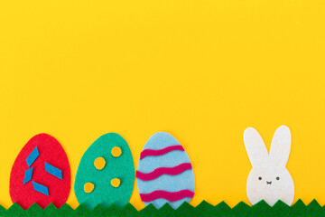 Easter holiday. Cut out of felt applications of eggs and a rabbit on the grass. Yellow background. Flat lay. Copy space