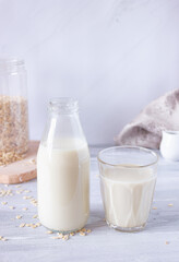 Vegetable oat milk in a glass bottle and in a glass cup on a light background. Healthy drinks, vegetarianism. Side view. Vertical photo
