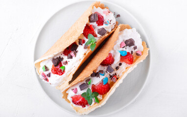 Sweet tacos with thin waffle, cottage cheese cream and strawberry topped with chocolate and mint on the white ceramic plate. Dessert variation of Mexican classics