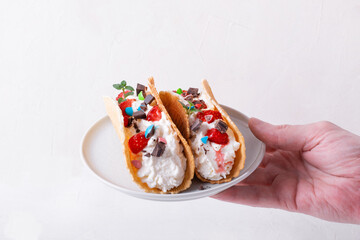 Sweet tacos with thin waffle, cottage cheese cream and strawberry topped with chocolate and mint on the white ceramic plate in man's hand