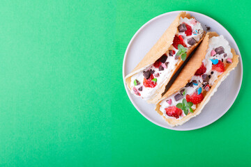 Sweet tacos with waffle, cottage cheese cream and strawberry on the white ceramic plate against the green background. Dessert variation of Mexican classics. Copy space