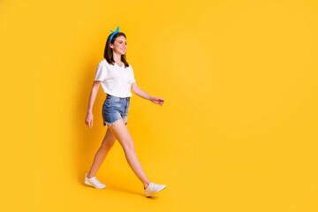 Fototapeta na wymiar Full body profile side photo of beautiful brown haired girl wear blue pin up white t-shirt good mod walk isolated on yellow background