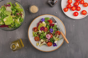 Vegetarian salad with tomato, lettuce, and cheese garnished with edible flowers and ingredients on a gray table. Spring food concept. 