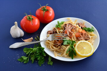 pasta with seafood and tomatoes on the white plate on the dark blue background