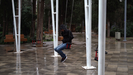 Lonely man in the park swinging on a swing. A sad man in depression is lonely swinging on a swing in an empty winter park.