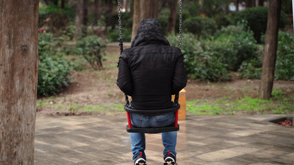 Lonely man in the park swinging on a swing. A sad man in depression is lonely swinging on a swing in an empty winter park.