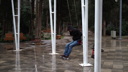 Lonely man in the park swinging on a swing. A sad man in depression is lonely swinging on a swing in an empty winter park.