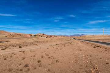 A small traditional village along a road in the Draa-Tafilalet region, with the Atlas Mountains on the background, in Morocco.