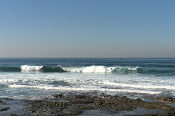 Surfer surfing the waves on a beach at La Jolla Tide Pools, San Diego, California in the afternoon on a sunny day in December; facing the Pacific ocean.