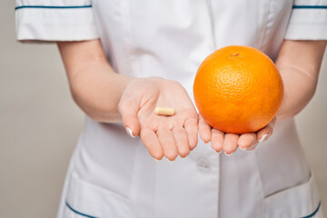 nutritionist doctor healthy lifestyle concept - holding orange fruit and nutrition vitamin capsules...