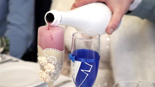 The man pours sparkling red wine into two glasses decorated in the style of the bride.