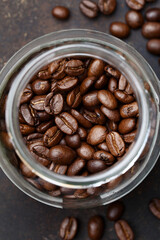 Roasted coffee beans in a jar over dark brown concrete background. Top view, selective focus