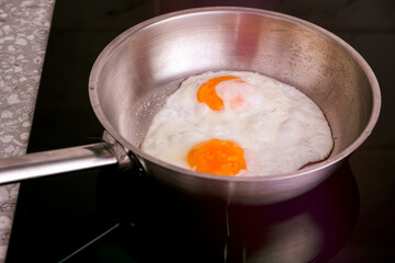 Two eggs in frying pan cooking on induction hob