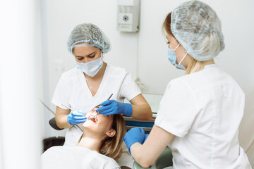 Medical treatment at the dentist office. Female dentist and assistant in dental office examining young woman with tools in dental clinic