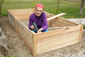 Woman screwing wooden frame for a raised garden bed.