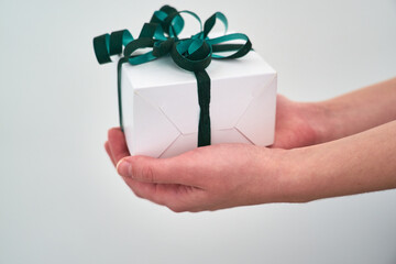 Female hands are holding a small gift wrapped in a green ribbon close-up on a white background.