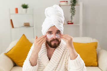 Bearded man applying eye patches on his face. Wrinkles and face home care for men.