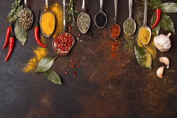 Assorted multicolored spices and herbs in vintage spoons on dark brown concrete background. Overhead view, copy space. Frame composition. Food background