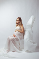 Fototapeta na wymiar Elegant pregnant young woman standing wearing flying white fabric. Pregnancy, maternity and motherhood concept.