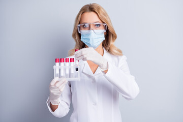 Portrait of lady nurse arms hold blood sample tubes wear safety facial mask isolated on grey color...