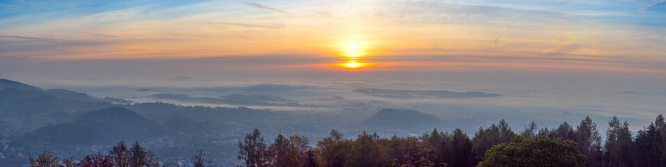 Amazing foggy sunrise over the city of Graz with Schlossberg hill and Church of the Sacred Heart of Jesus tower, in Styria region, Austria. Panoramic view from Plabutsch mountain on autumn morning.