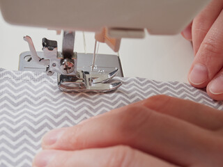 Sewing process, close up seamstress hands sew white clothes with sewing machine.