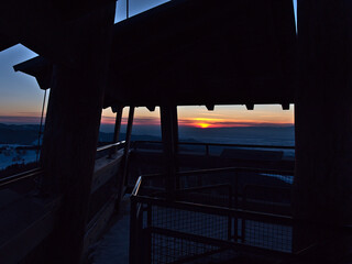 Beautiful sunset in winter viewed from the top of wooden observation tower Eugen-Keidel-Turm on Schauinsland peak in Black Forest, Germany, with the silhouettes of railing and observation deck.