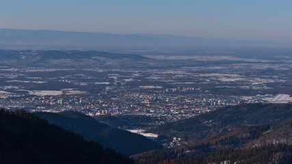Fototapeta premium Beautiful aerial view of city Freiburg im Breisgau, Kaiserstuhl hills and Vosges mountain range on horizon in winter with snow-covered landscape viewed from Schauinsland peak, Black Forest, Germany.